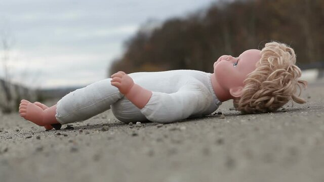 The childish doll lies on the side of the road.