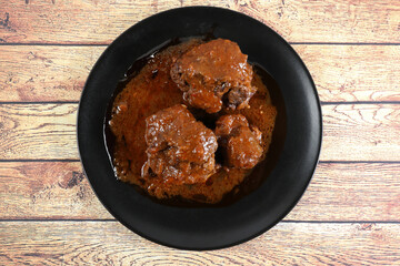 Ration of bullfighting oxtail stewed in black plate, on wooden table