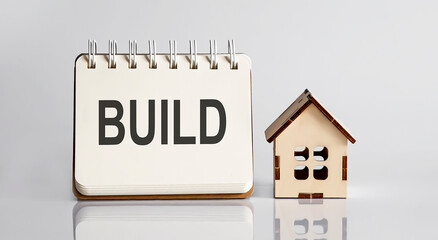 BUILD words written in an office notebook with wooden house. Financial Business concept.