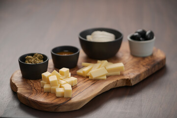 Wood board with cheese, olives and sauces on walnut table