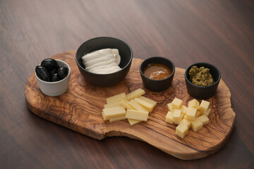 Wood board with cheese, olives and sauces on walnut table
