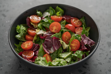 Salad with green and purple leaves and cherry tomatoes in black bowl
