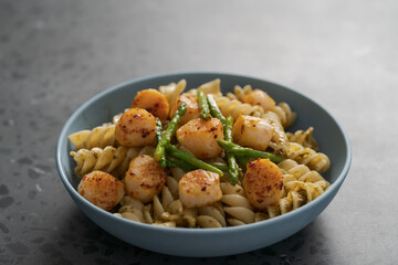 Fusilli pasta with scallops and asparagus in blue bowl on concrete surface