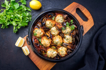 Traditional Norwegian fish ball fiskeboller with fish and mussels in red wine sauce as top view in a modern design pot