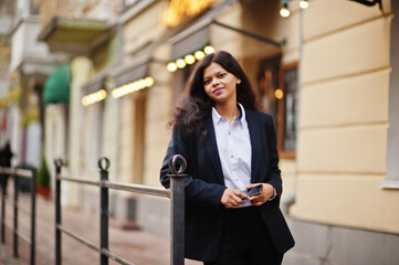 Gorgeous indian woman wear formal posing at street with mobile phone at hands.