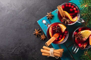 Hot wine with spices and fruits in a glass on a black textured background and branches of a Christmas tree, top view. Alcoholic hot drink for the holiday.