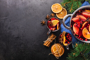 Mulled wine or punch in a glass and hot wine in a cooking pot with spices and fruits on a black...