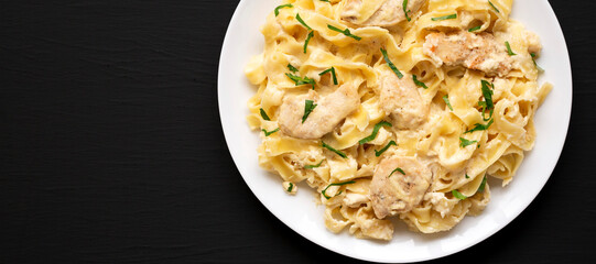 Homemade Chicken Fettuccine Alfredo on a white plate on a black background, top view. Flat lay, overhead, from above. Space for text.
