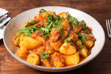 Greek vegetable stew of potatoes and vegetables in tomato sauce in a plate on a wooden table, top view, close-up