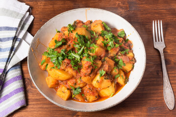 Greek vegetable stew of potatoes and vegetables in tomato sauce in a plate on a wooden table, top view, close-up