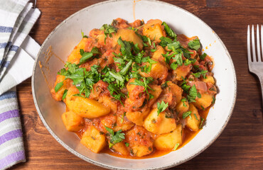 Greek vegetable stew of potatoes and vegetables in tomato sauce in a plate on a wooden table, top view, close-up