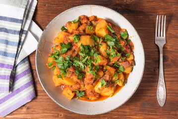 Greek vegetable stew of potatoes and vegetables in tomato sauce in a plate on a wooden table, top view, close-up