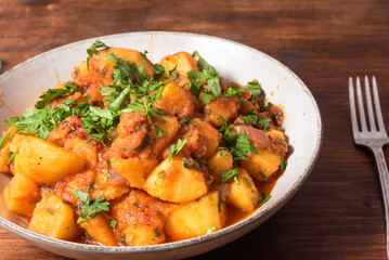 Greek vegetable stew of potatoes and vegetables in tomato sauce in a plate on a wooden table, top view, close-up