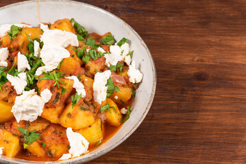 Greek vegetable stew of potatoes and vegetables in tomato sauce with chunks of soft feta cheese in a plate on a wooden table, top view, copy space