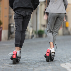 Rear view of unrecognizable trendy fashinable teenagers riding public rental electric scooters in...