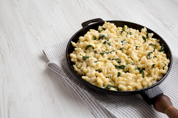 Homemade Spinach Mac and Cheese in a cast-iron pan on a white wooden background, side view. Copy space.