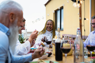 Happy multiracial senior friends having fun dining together on house patio - Elderly lifestyle people and food concept