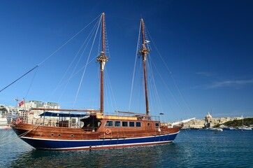 Obraz premium Cruise sailboat in the port of Tas Sliema, Valletta, Malta. A wooden sailboat waits in the harbor on a sunny day on the calm sea.