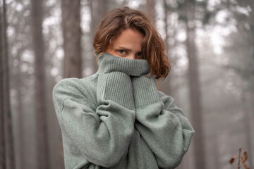 Happy woman in warm cozy green sweater in beautiful pine forest hiding face