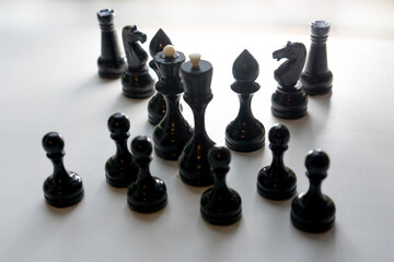 Wooden chess pieces. Black king Queen surrounded by her large retinue, full set of black side chess game, counter light, all pieces in shadow