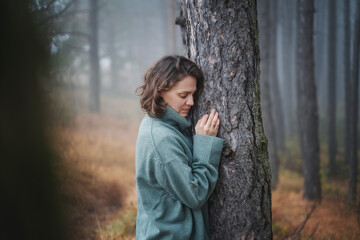 Happy woman in warm cozy green sweater in a beautiful foggy pine forest