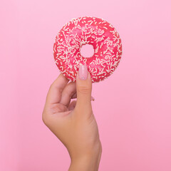 Female hand with pink manicure nails holding strawberry donut