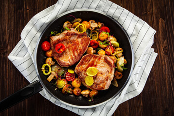 Pork steaks in frying pan with champignons, onion and tomatoes

