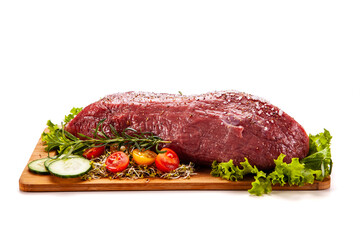 Fresh raw beef on cutting board with fresh vegetables on white background
