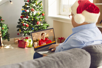Granddad in Santa hat sitting on sofa at home on Christmas Day and video-calling his grandson