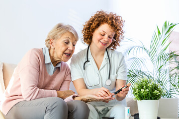 Happy senior woman having her blood sugar measured in a nursing home by her caregiver. Happy nurse measuring blood sugar of a senior woman in living room - diabetes and glicemia concept