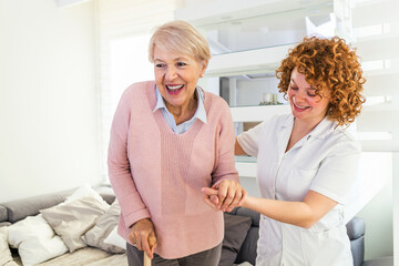 Smiling nurse helping senior lady to walk around the nursing home. Portrait of happy female caregiver and senior woman walking together at home. Professional caregiver taking care of elderly woman.