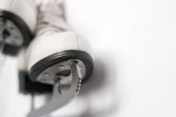 White figure skates with silver blades close-up hang against white wall background
