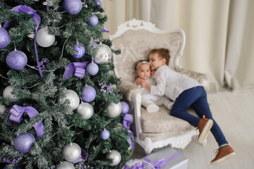 Selective focus on tree. In background are two kids brother and sister are sitting on a vintage armchair in a white room