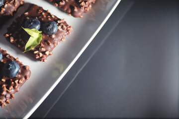 Chocolate dessert with nuts and fresh berries. Sweet snack for coffee biscuit in glaze and nut crumbs with fruit.