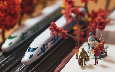 Miniature toy figurines of alone woman waiting at a high speed train platform in autumn or fall season concept -  warm tone filter applied.