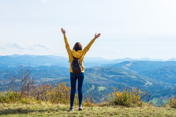 Girl in a yellow hoodie, with her hands up, on the top of a mountain. Success.