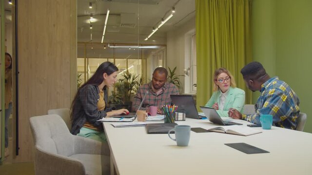Strict displeased african american male boss scolding pretty asian female employee for being late at business team meeting, giving rebuke while diverse multiethnic colleagues working in boardroom.