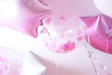 Pink, white and transparent balloons with rose petals inflated with helium on a white background