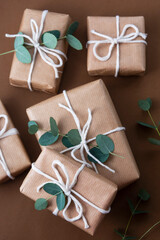 Christmas gift boxes wrapped with brown kraft paper and decorated with eucalyptus leaves, over brown background. Top view.