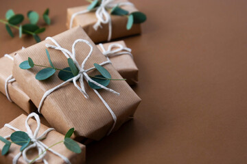 Christmas gift boxes wrapped with brown kraft paper and decorated with eucalyptus leaves, over brown background. Top view.