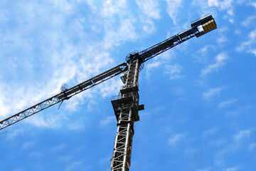 Crane. Big tower construction crane against blue cloudy sky. Construction site.