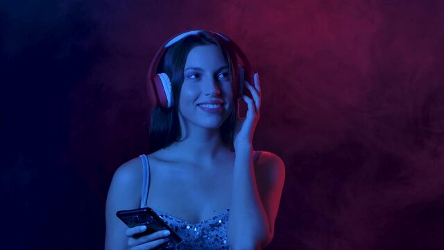 Portrait of charming young woman enjoying music from smartphone in big red headphones. Close up. Slow motion.