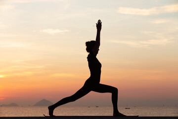 Silhouette of a young woman doing yoga near the sea at sunset.