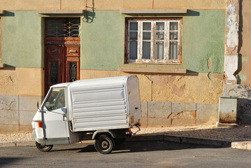 Small White Delivery Van Parked on Road Beside Old Building 