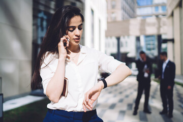 Pensive ethnic woman checking time on wristwatch