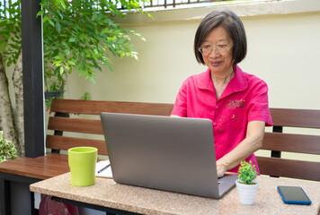 senior reitred asian woman using computer to write email and sitting at home