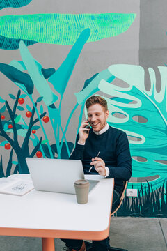 Young Businessman Sitting at Cafe and Talking on his Cell Phone