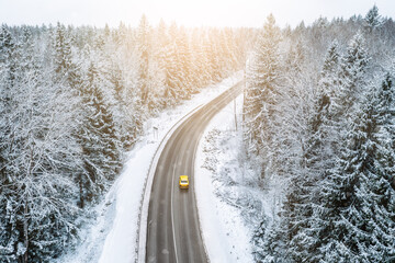 Aerial view of winter road with car and snow covered trees in the forest