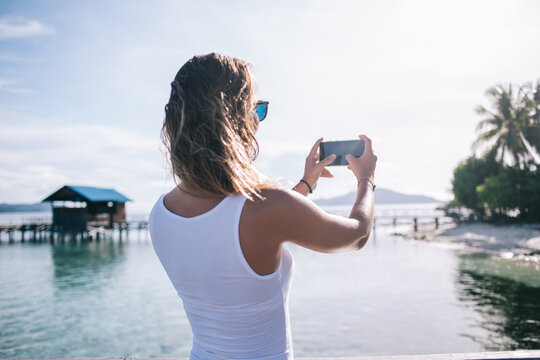 Female blogger with modern mobile gadget focus camera clarity for making good content images during getaway travelling for visiting Hawaii Environment, millennial woman shooting live streams video