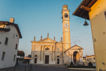 Obraz premium Old medieval cathedral with bell tower and the clock on it in the sunset time. Beautiful italian church. San Paolo.Chiesa di Santa Maria Nascente
